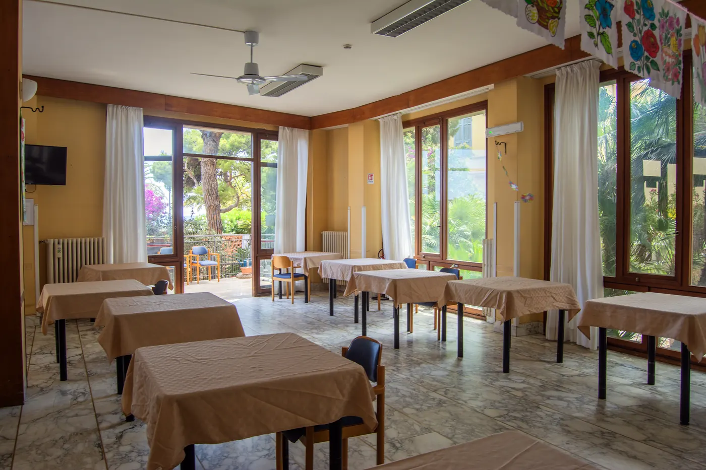Sala da pranzo luminosa con grandi vetrate della RSA Le Palme